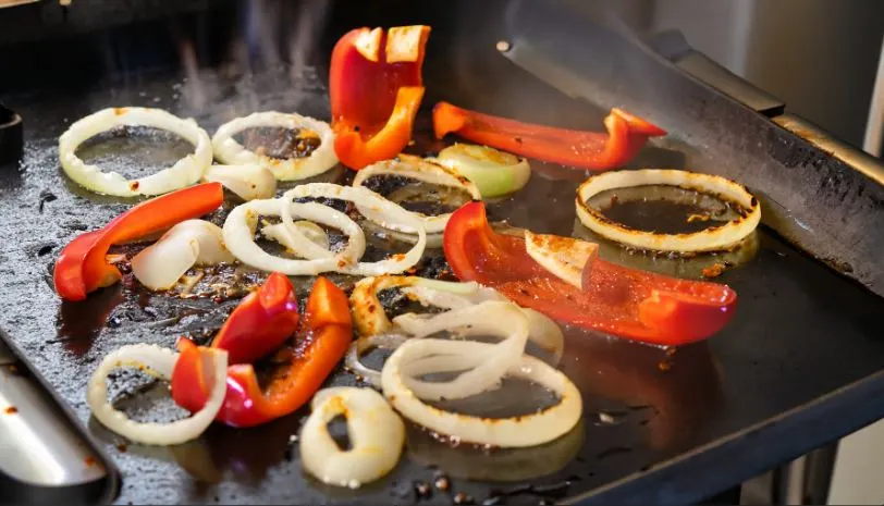 Onions and peppers sizzling on a hot griddle as theyre being smashed for flavorful burgers