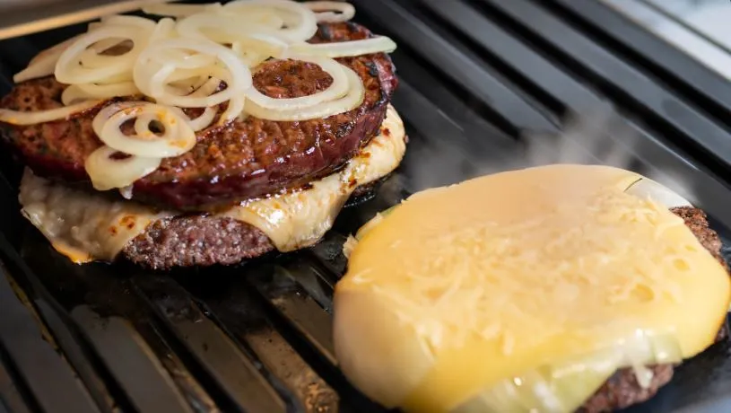 Onions sizzling on a hot griddle next to a melting slice of cheese ready to top the sizzling patty for the Oklahoma Onion Smashburger